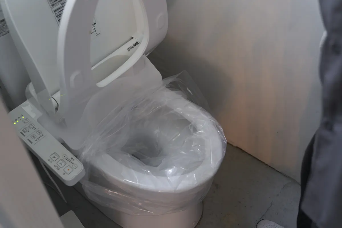 洋式便器に半透明の養生シートをかぶせているところ。